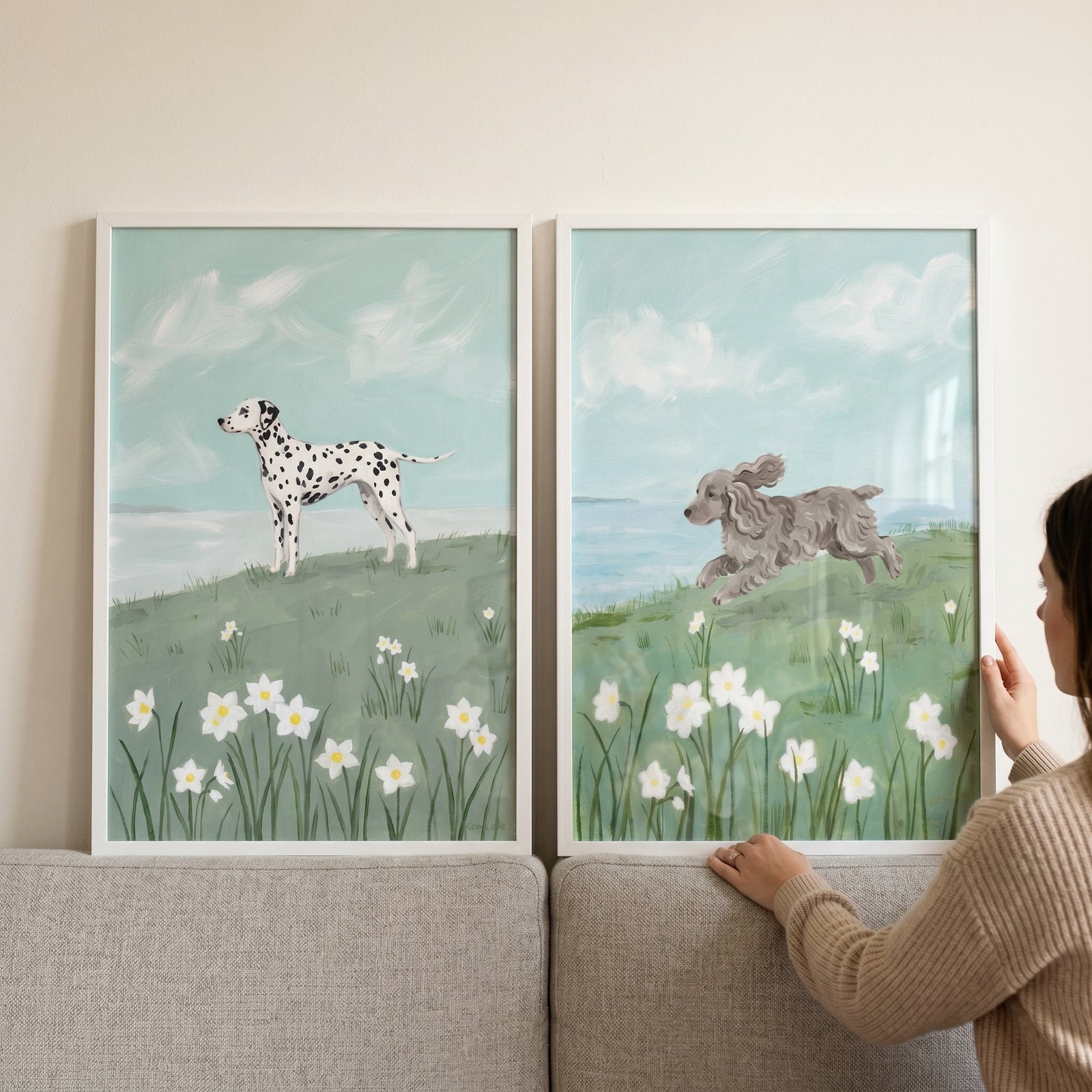 Woman holds this botanical spring daffodil dogs wall art set of 2 featuring a Dalmatian and a grey dog in a meadow.
