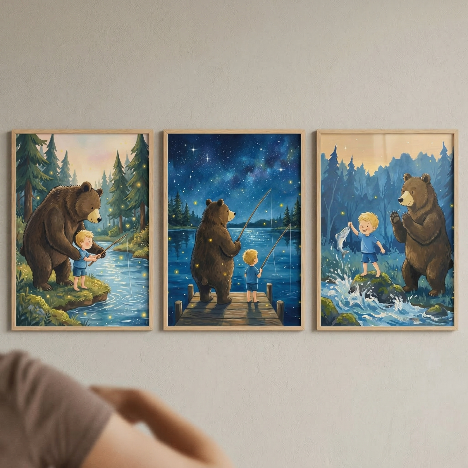 Three framed vertical illustrations are displayed side-by-side on a light-colored wall, depicting a whimsical friendship between a large brown bear and a small blonde boy.

The left panel shows the pair on a grassy riverbank during the day. The bear stands behind the boy, who wears a blue t-shirt and shorts, helping him hold a fishing rod over a flowing stream. The background features a dense pine forest under a soft, glowing sky, with small fireflies scattered throughout the scene.

