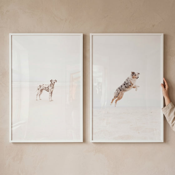 Bright minimalist coastal dog wall art set of 2 featuring a Dalmatian standing and a shepherd jumping on a sandy beach.