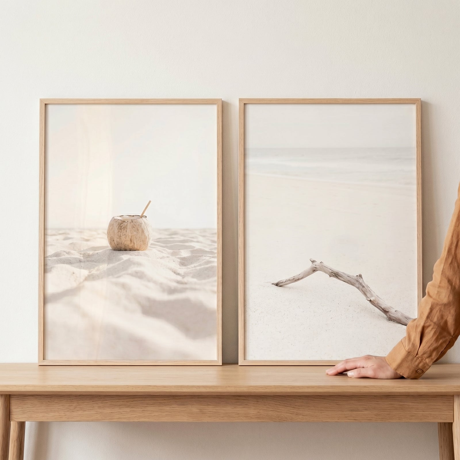 Bright minimalist white beach wall art set of 2 with a coconut and driftwood in light wood frames on a table with a hand.