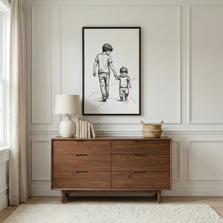 Framed sibling wall art displayed above a wooden dresser in a bright, elegant room, showing an older child walking hand-in-hand with a younger one. The clean, emotional line art adds warmth and meaning to family-inspired wall art collections.