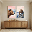Two framed watercolor prints of brown bears hanging above a light wood changing table in a neutral nursery. The left print features a close-up profile of a bear, and the right shows a bear standing on a rocky mountain peak, both against pink skies and blue mountains.