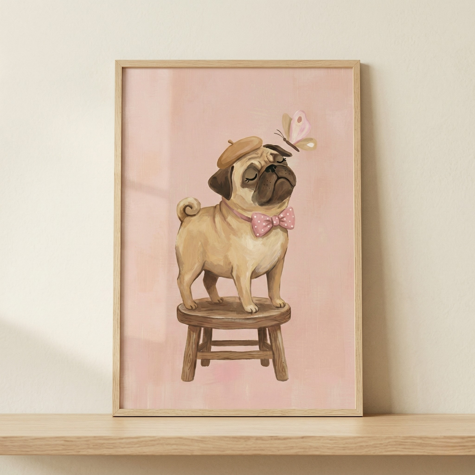 A framed illustration of a small tan dog with a wrinkled face standing on a wooden stool. The dog wears a matching tan beret and a pink bow tie with white polka dots. Its eyes are closed in a serene manner as a delicate pink butterfly flutters near its snout. The artwork is set against a solid pastel pink background and is housed in a light-colored wooden frame. The entire piece rests on a smooth wooden shelf against a plain, neutral-toned wall.