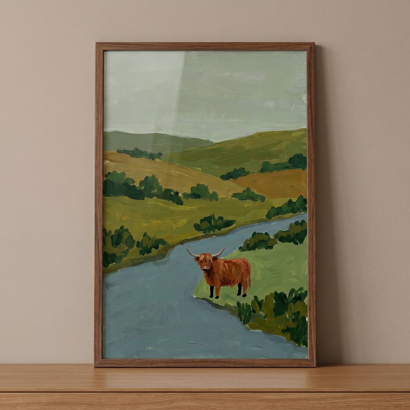 Brown shaggy highland cow wall art in a wood frame features a cow by a blue river and soft hills under a pale green sky.