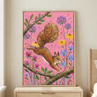 A vertical framed illustration of a nimble brown squirrel captured mid-leap between textured tree branches. Its large, bushy tail is rendered with detailed golden-brown highlights. The scene is set against a vibrant pink background adorned with multicolored speckles. Various whimsical flora, including yellow daisies, blue wildflowers, and pink clover-like blooms, fill the space around the squirrel. This bright artwork is encased in a light wood frame and displayed atop a wooden nightstand.