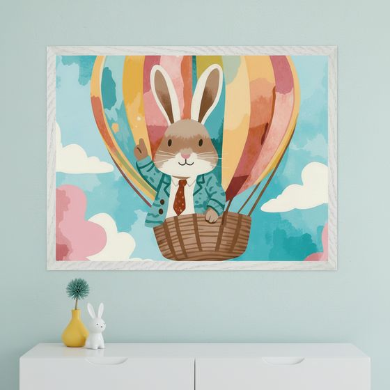Modern room with a light blue wall and a white dresser. A framed watercolor-style artwork of a brown rabbit in a teal suit and red tie riding a colorful hot air balloon hangs centered above the dresser. A yellow vase with a teal flower and a white ceramic bunny are on the dresser.