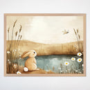 A sweet illustration depicting a soft brown bunny sitting peacefully by a small pond, watching a dragonfly flutter nearby. The scene, accented with gentle daisies and natural grasses, evokes tranquility and is ideal for nursery or children's room decor.