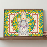 Close-up of a framed illustration showing a serious gray bunny in western attire centered within a red and cream scalloped frame over a bright yellow cheetah-print backdrop. This colorful and quirky wall art creates a standout statement in any room.