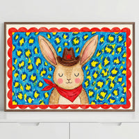 Framed bunny wall art featuring a smiling rabbit with oversized ears in a western outfit, surrounded by a vivid animal print background. The vibrant colors and bold patterns give this wall art a fun and energetic personality.