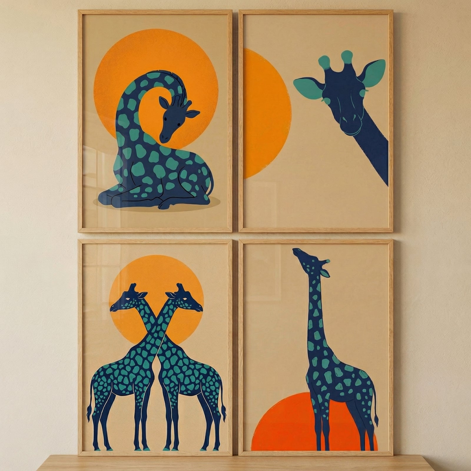 A set of four minimalist graphic illustrations, each in a light wood frame, is displayed in a 2x2 grid on a neutral-colored wall. The artwork features stylized giraffes in a dark blue hue with teal spots, set against a light tan background. Each piece includes a large, solid orange circle representing a sun.
