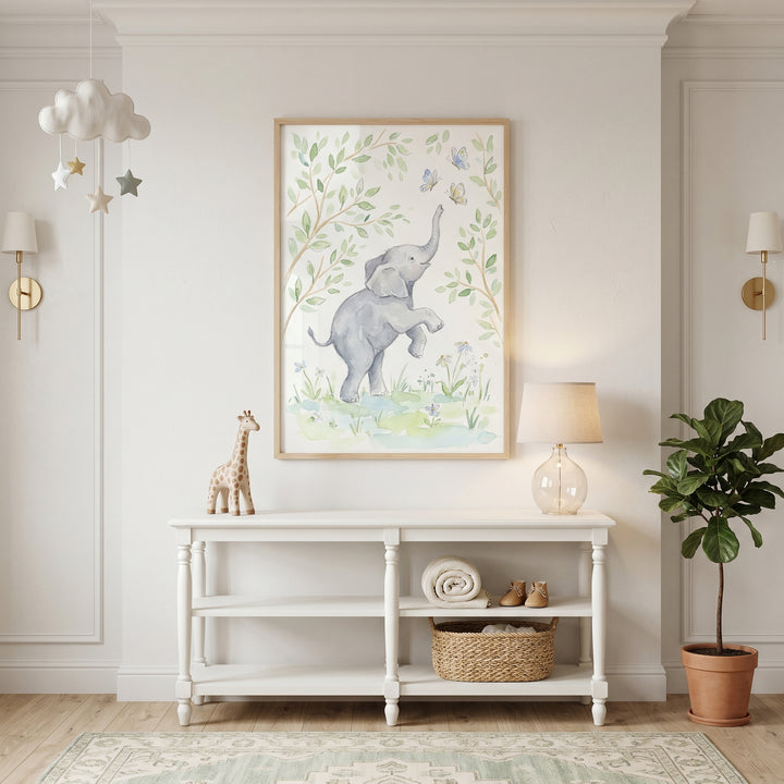 Framed butterfly baby elephant wall art above a white console table in a neutral nursery with a toy giraffe.