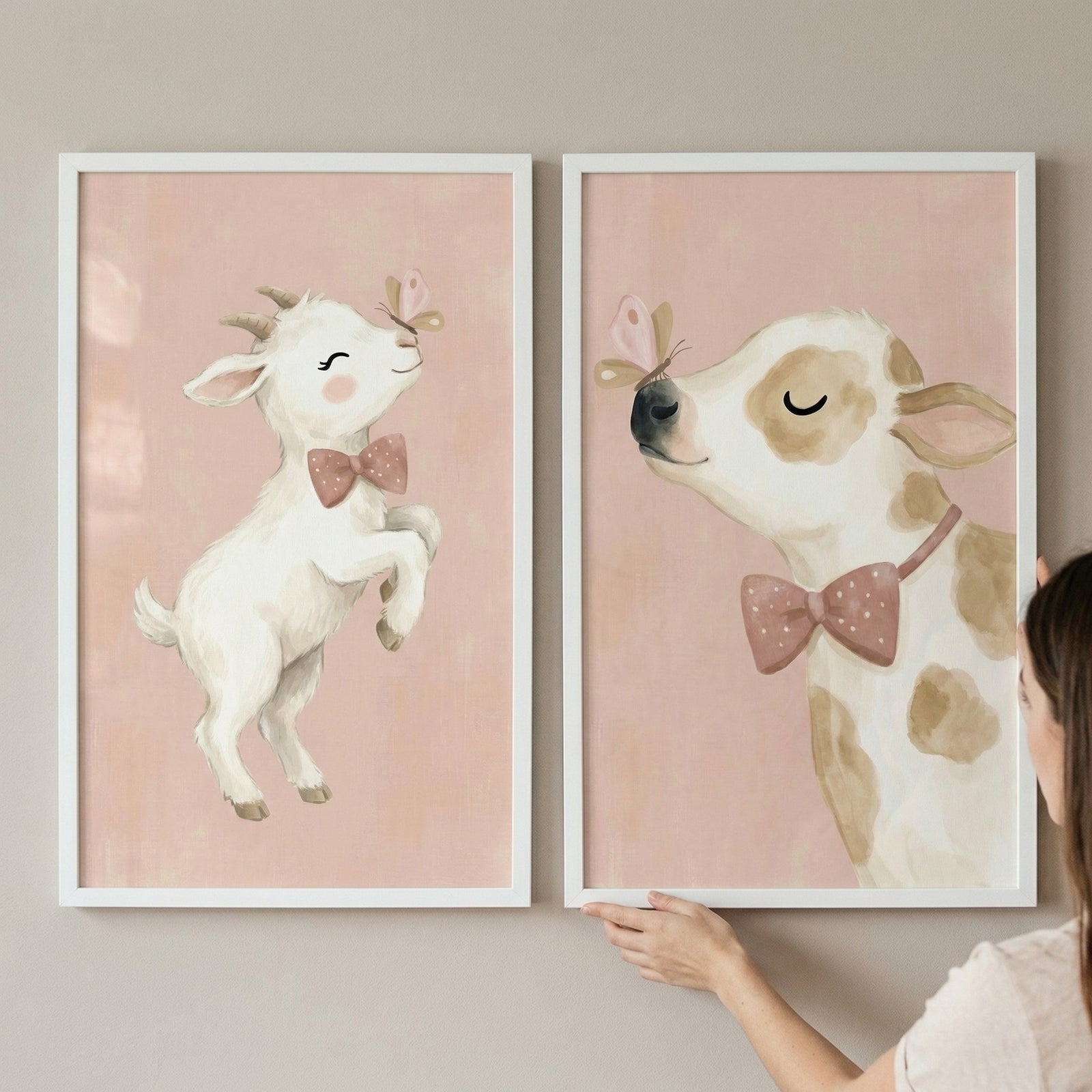 Two white-framed wall prints are held against a neutral wall. The left print shows a whimsical, white baby goat with tiny horns and rosy cheeks, wearing a pink-and-white polka-dot bow tie. The goat jumps playfully near a small pink butterfly. 