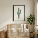 Framed cactus print with soft desert tones hanging above a wooden crib in a neutral-toned nursery. The botanical artwork adds a peaceful, nature-inspired touch to the space.
