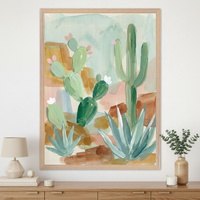 Modern living room with a light wood dresser. A large framed loose watercolor painting of desert cacti and succulents hangs above the dresser. A lamp, books, and a vase with greenery are on the dresser.