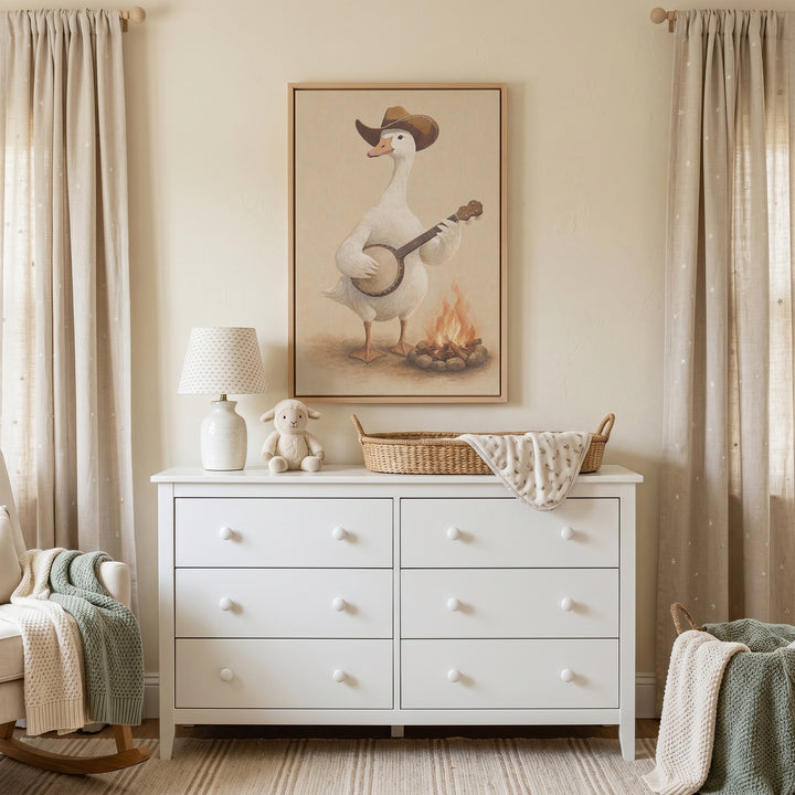 Campfire banjo playing goose wall art above a white dresser with a lamp and changing basket in a neutral nursery.