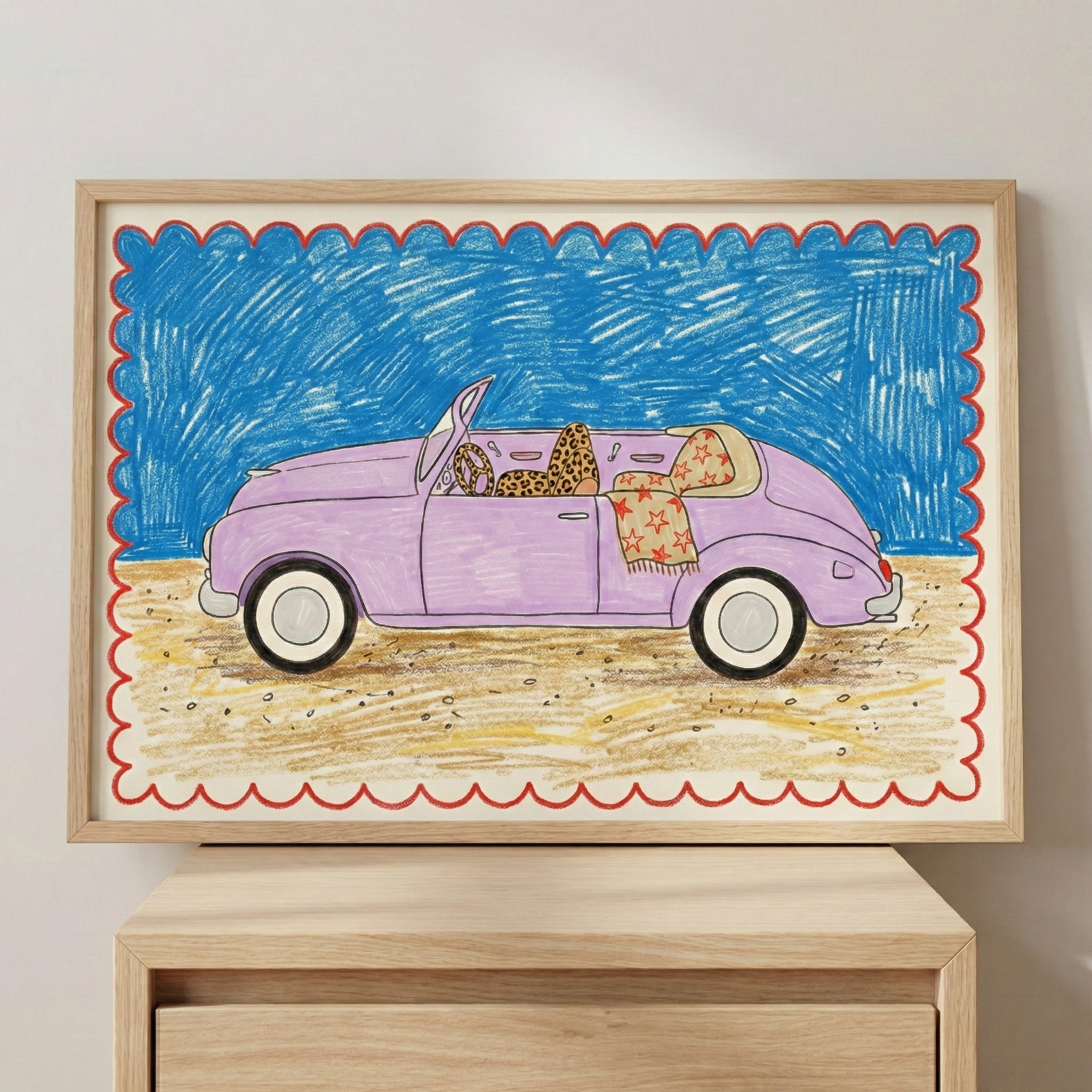 A framed drawing of a lavender convertible car with leopard-print and star-patterned seat covers, parked on a sandy beach under a vibrant blue sky, bordered by a red scalloped frame. The artwork has a playful, crayon-like style and rests on a wooden surface.