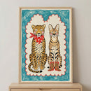 Whimsical illustration of a serval and a leopard sitting side by side, both with pink cheeks and closed eyes. The leopard wears a red star-patterned bandana, and the serval sports red cowboy boots. The image is framed with bold crayon-like blue and red borders, giving it a playful, childlike charm.
