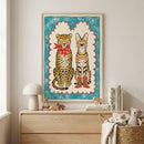 Framed drawing of a leopard in a red bandana and a serval in cowboy boots displayed above a wooden dresser in a cozy, minimalist room. The dresser holds books, wooden animal toys, and a mushroom-shaped lamp, with a woven basket and stuffed bear beside it, creating a warm, child-friendly space.