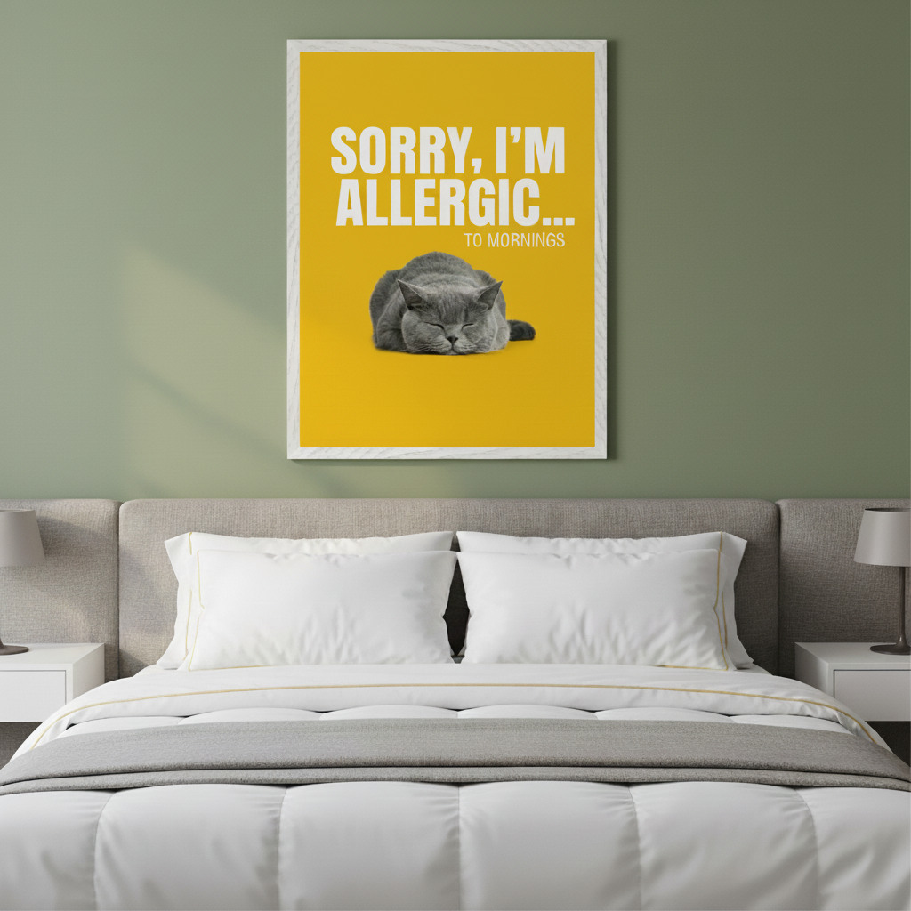 Modern bedroom with a gray upholstered bed and two white nightstands. A large framed yellow poster with white text "SORRY, I'M ALLERGIC... TO MORNINGS" and a sleeping gray cat is centered above the bed.