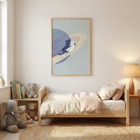A cozy, minimalist child's bedroom features neutral and pastel tones. A light-wood bed frame is dressed in cream linens and a soft pink duvet. Above the bed hangs a large framed artwork depicting two cats, one black and one white, cuddling on the rings of a blue planet. To the left, a wooden shelf holds colorful books and teddy bears. A large grey knitted elephant and more plush toys sit on a circular woven rug. A simple wooden lamp on a side table casts a warm glow.