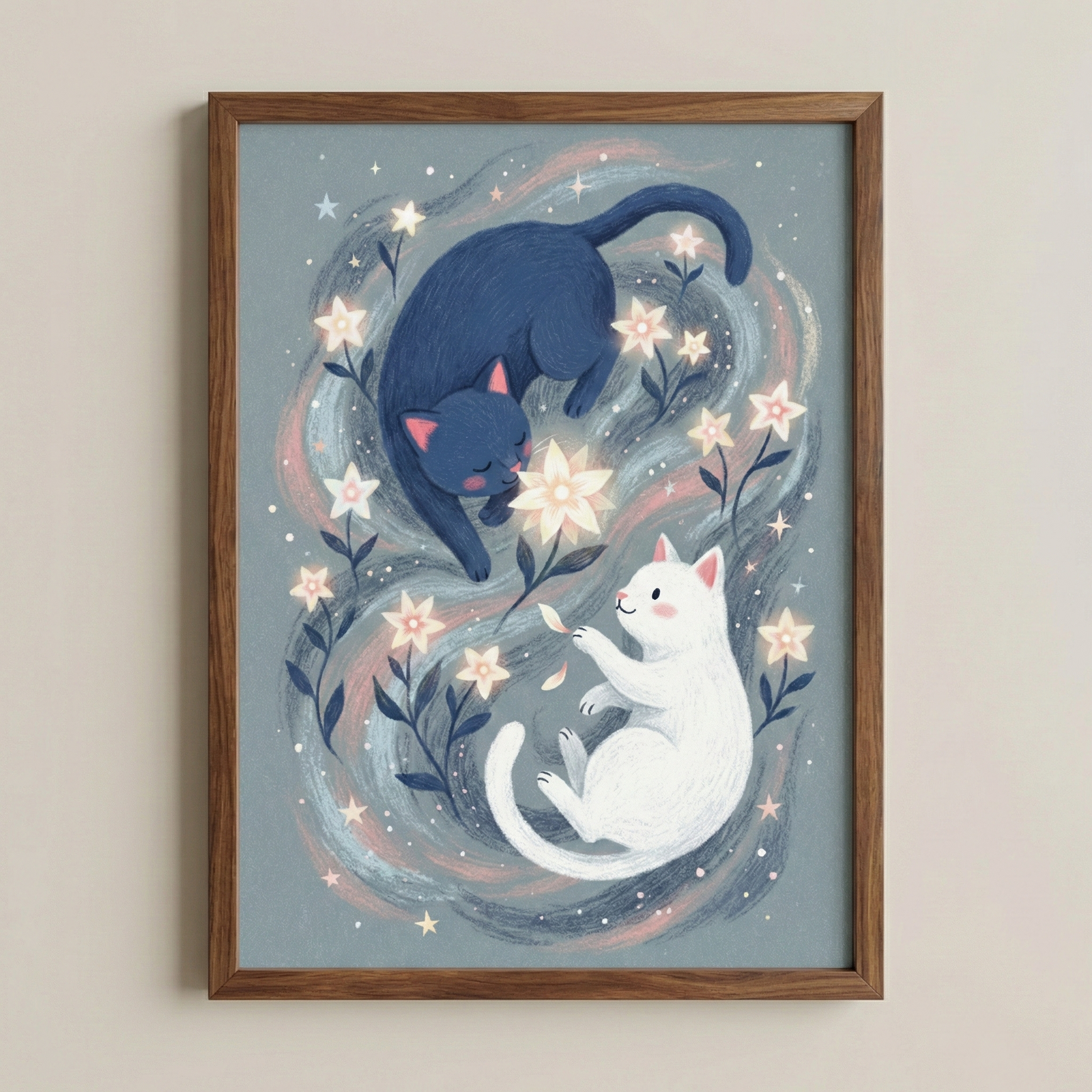 A framed illustration shows two cats in a cosmic scene. At the top, a dark blue cat curls around a large, glowing white flower. Below, a white cat floats on its back, reaching for a falling petal. Both are surrounded by swirling blue and pink wisps. Star-shaped white flowers and tiny twinkling stars are scattered throughout. The whimsical art has a soft, textured style and is held in a light brown wooden frame against a plain wall.