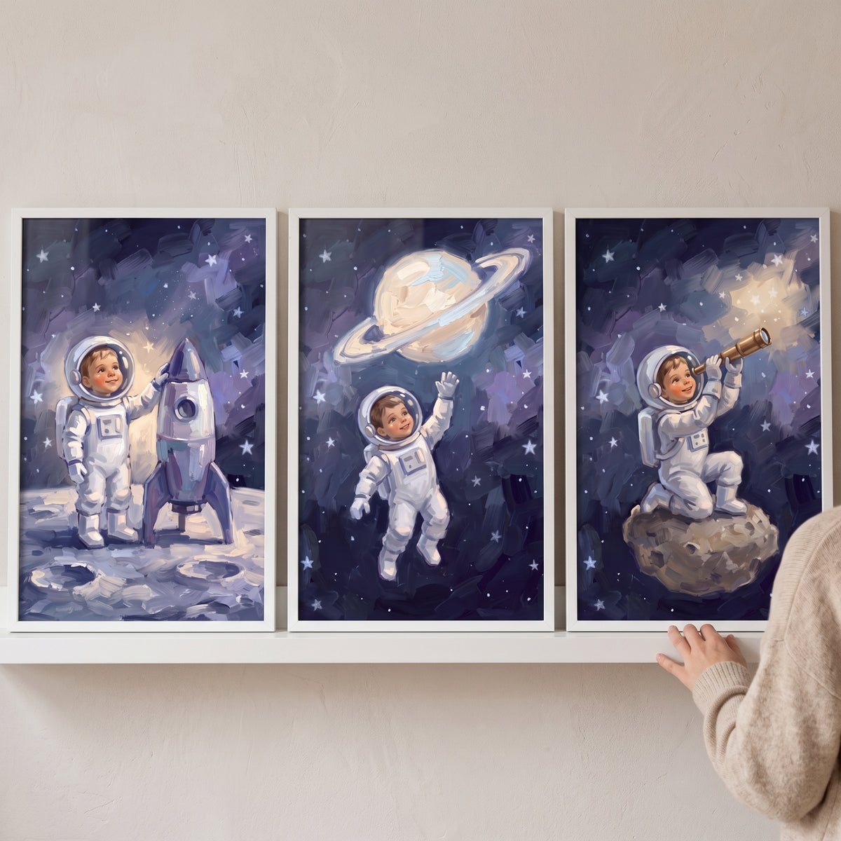 Celestial navy baby astronaut wall art set of 3 shows a child in space with a rocket ship, ringed planet and telescope.