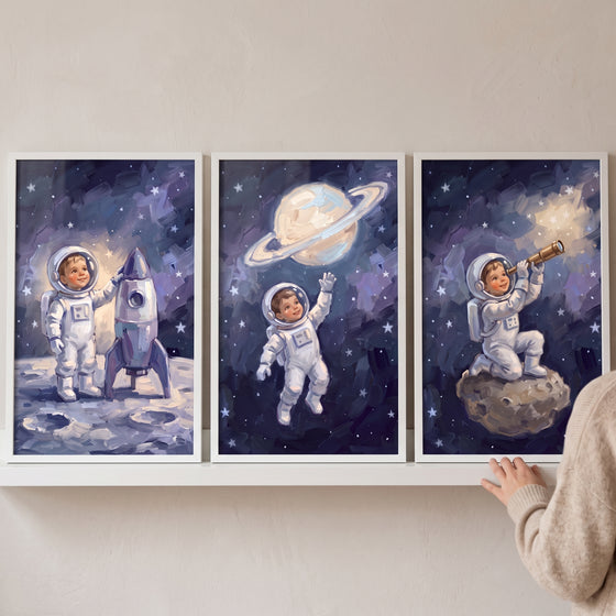Celestial navy baby astronaut wall art set of 3 shows a child in space with a rocket ship, ringed planet and telescope.