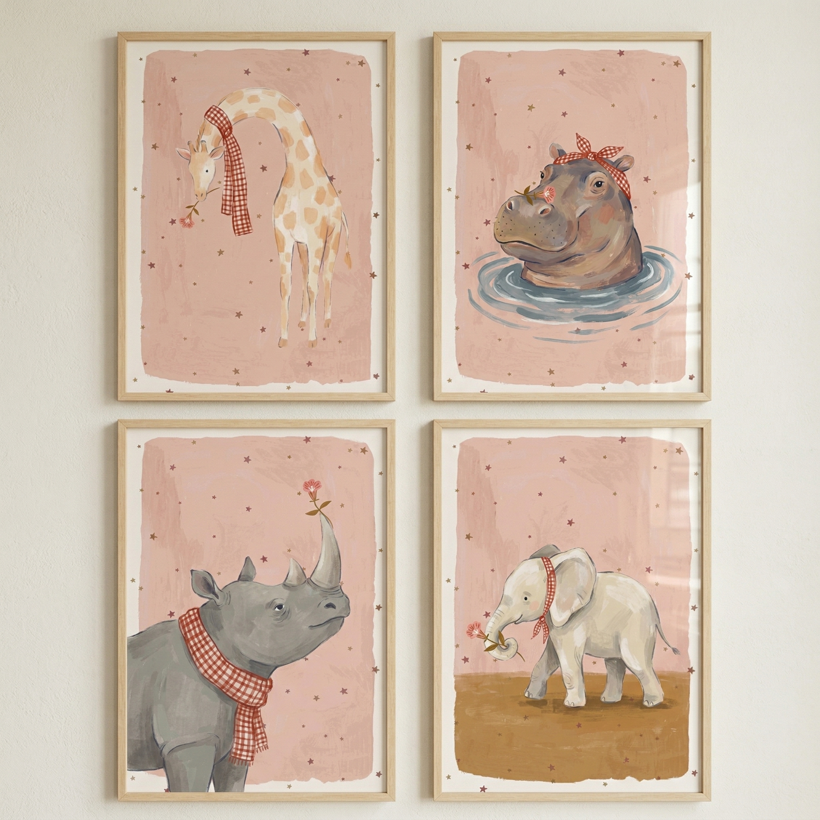 Four framed pastel animal illustrations arranged in a grid show a giraffe, hippo, rhino, and elephant each wearing red checkered accessories and holding small flowers. The soft pink star patterned backgrounds and matching style create a coordinated nursery wall art set with a gentle, whimsical feel.