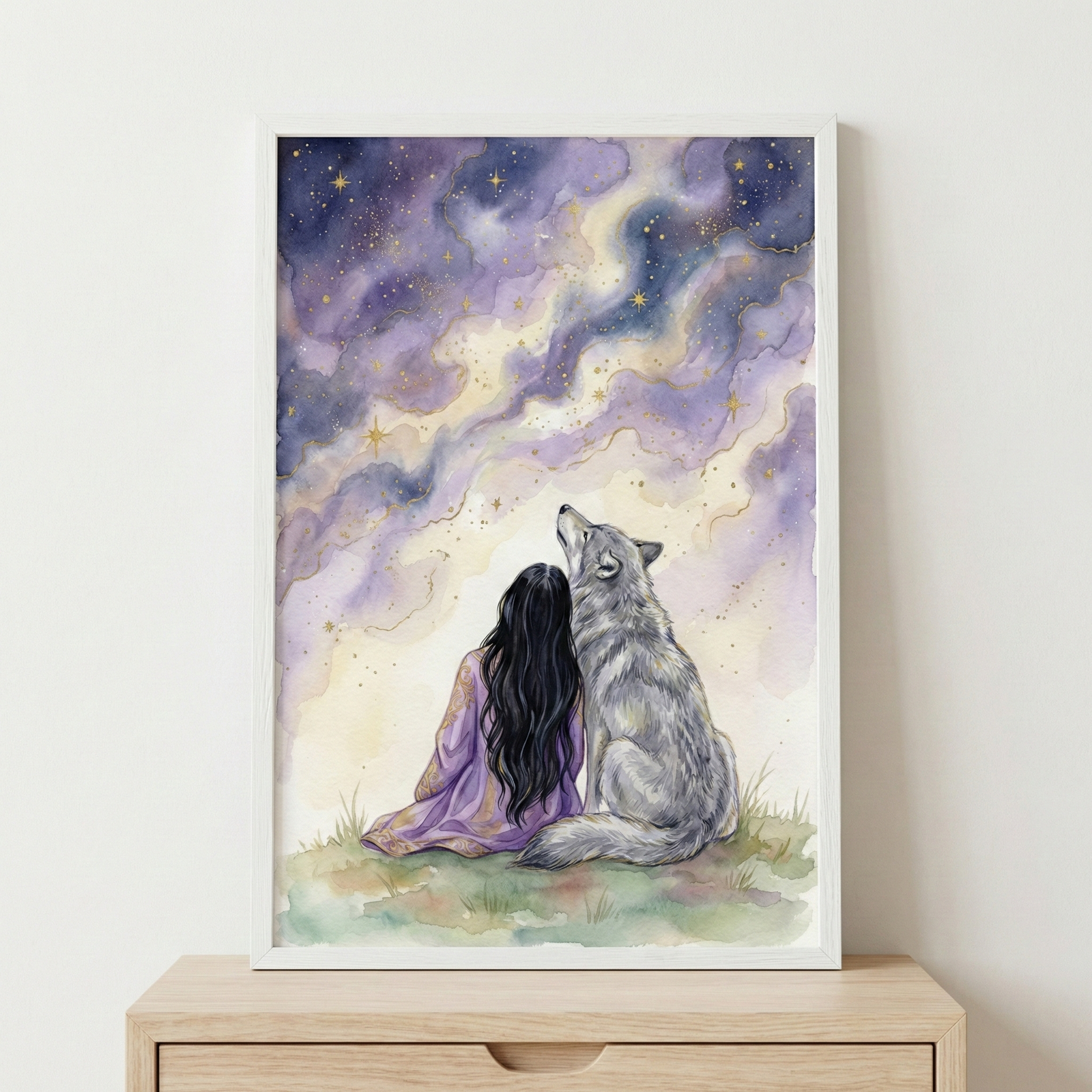 A framed watercolor-style illustration sits on a wooden surface. The artwork features a woman with long dark hair and a wolf sitting together on a grassy hill, viewed from behind. They are gazing up at a dreamy night sky filled with swirling purple, blue, and yellow clouds. Golden stars and shimmering lights are scattered across the celestial expanse. The woman wears a soft purple garment, and the wolf is detailed with grey fur. The scene conveys a sense of wonder and companionship.