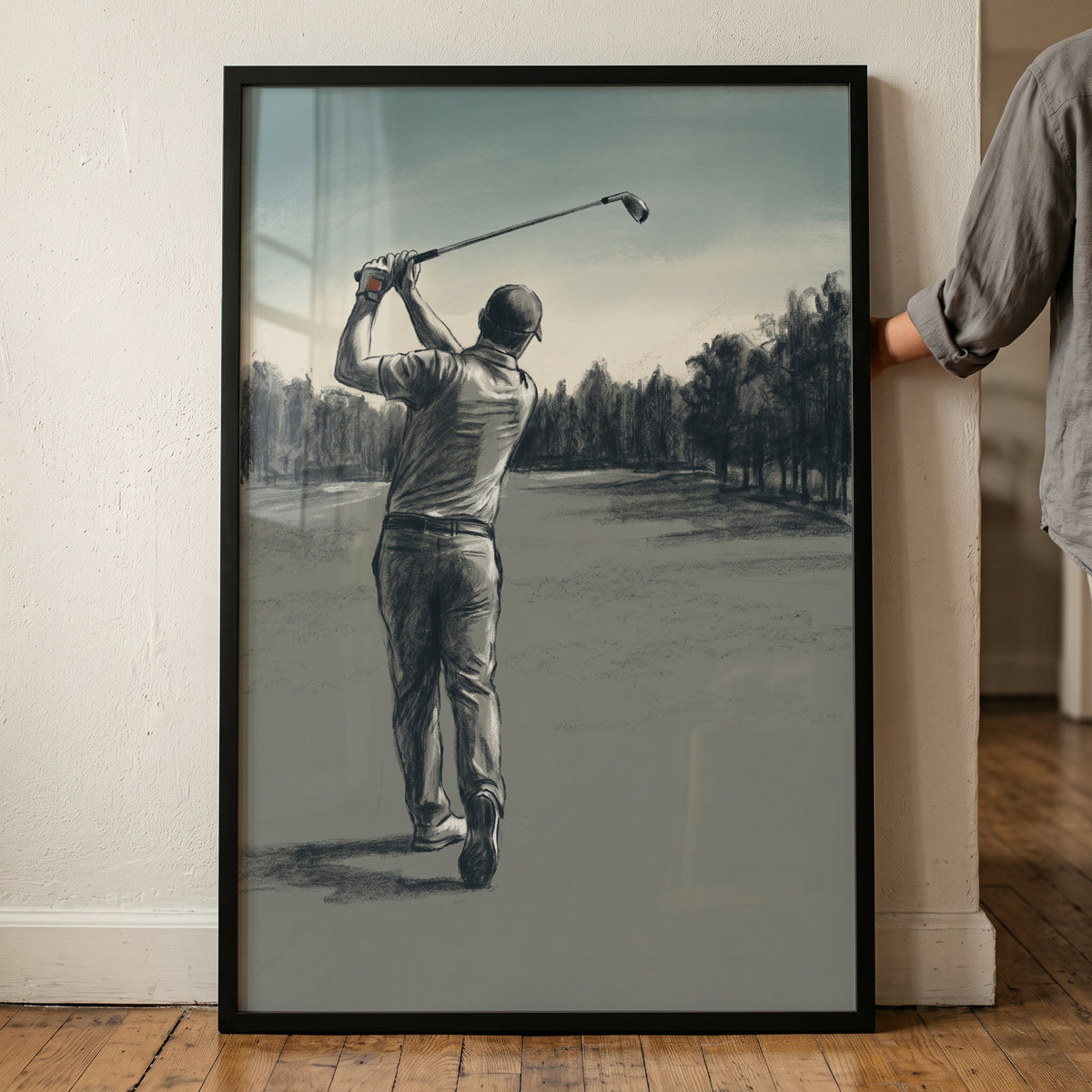 Framed charcoal swing golfer sports wall art depicts a man finishing his golf swing on a treelined course.