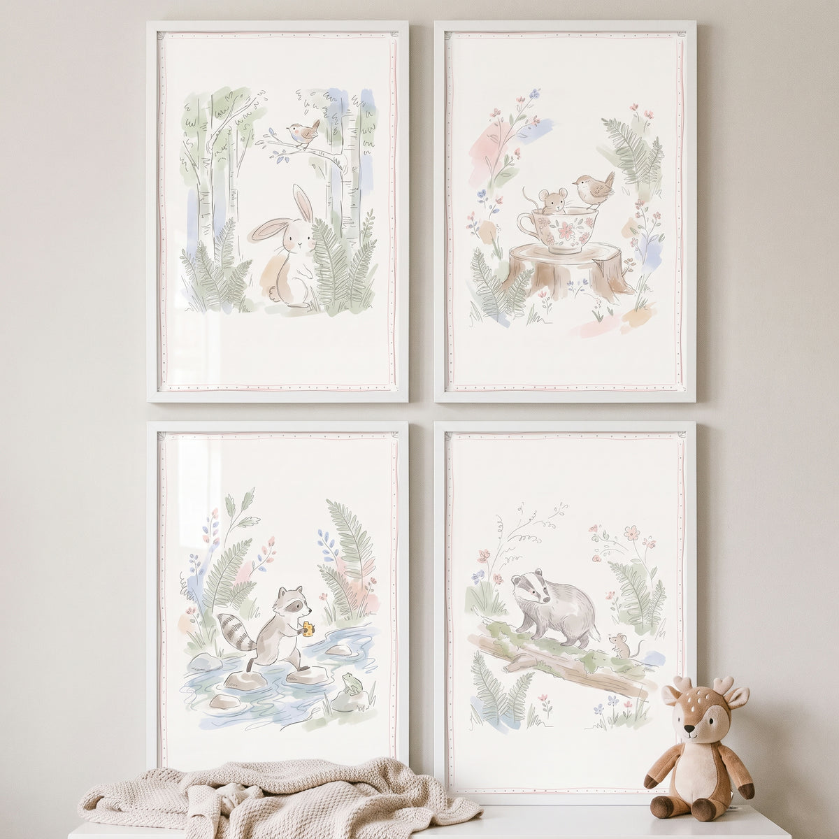 Charming pastel forest animal wall art set of 4 in white frames above a baby blanket and plush deer toy.