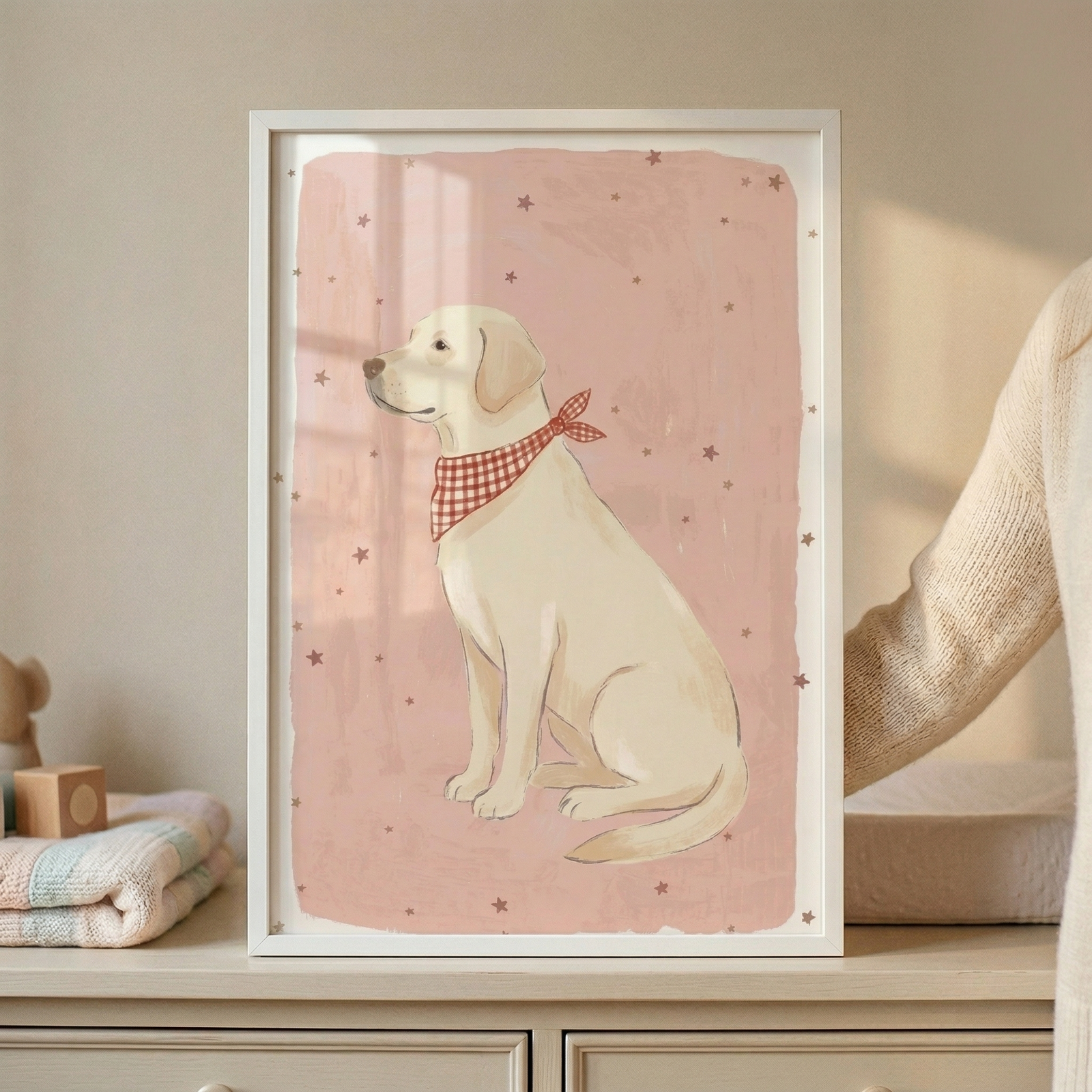 This image shows a digital illustration of a cream-colored, sitting dog in profile. The dog is wearing a red and white checkered bandana around its neck. It is set against a soft, muted pink background that features small, dark star shapes scattered throughout. The artwork is presented in a simple white frame, which is resting on a light-colored wooden surface. 