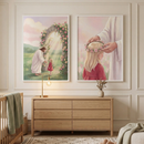 A bright and airy bedroom interior featuring two framed illustrations on a neutral wall. The illustration on the left shows Jesus Christ walking hand-in-hand with a young girl in a red dress through a path of blooming pink trees. The illustration on the right is a close-up of Jesus Christ placing a flower crown on the same young girl's head. Below the art, a light wood six-drawer dresser holds a few wooden toys and a small white lamp. A woven basket sits on a white rug near a long white curtain.