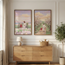 Two framed vertical illustrations hang side-by-side on a white paneled wall above a light wood dresser with six drawers. The illustration on the left shows Jesus Christ sitting on a wooden bench next to a young girl in a red dress, set in a field of light purple flowers under a soft pink and blue sky. The illustration on the right depicts Jesus walking hand-in-hand with the same young girl down a path lined with blossoming trees. On the dresser sits a small lamp and a woven basket containing stuffed toys. 