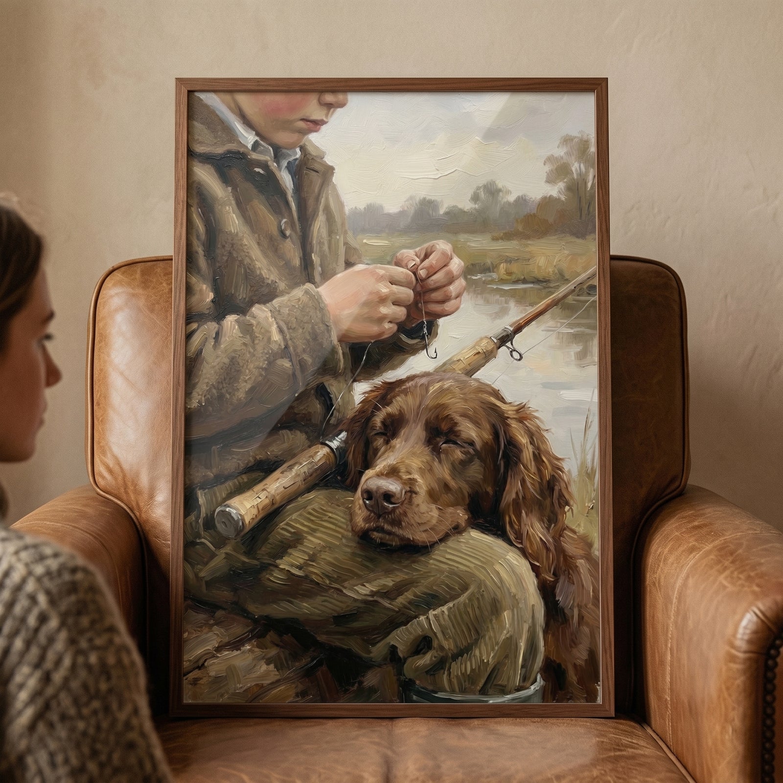 Classic riverside country boy wall art of a boy with his dog by a river, framed and resting on a brown leather armchair.