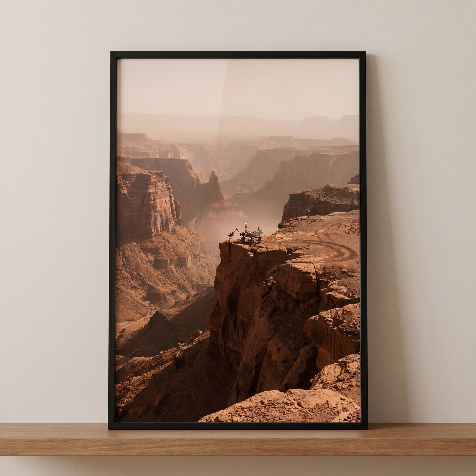 Framed cliff edge mars rover wall art on a shelf depicts a vehicle overlooking a hazy, vast reddish rocky canyon.
