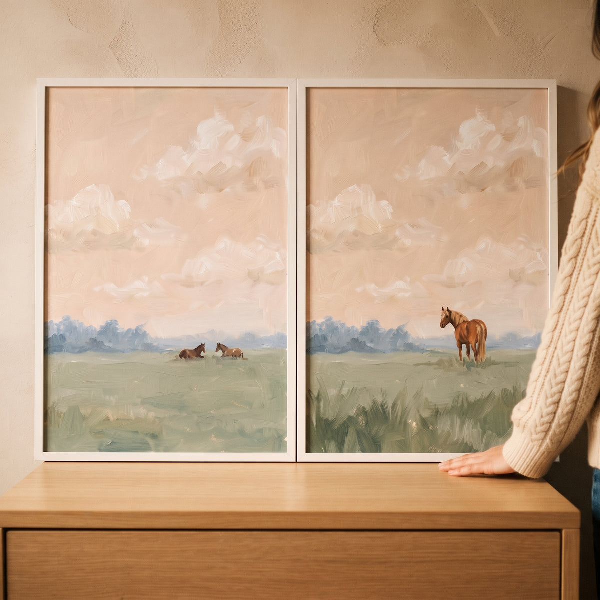 Cloudy apricot sky horses wall art set of 2 showing horses in a green field rests on a wooden dresser.