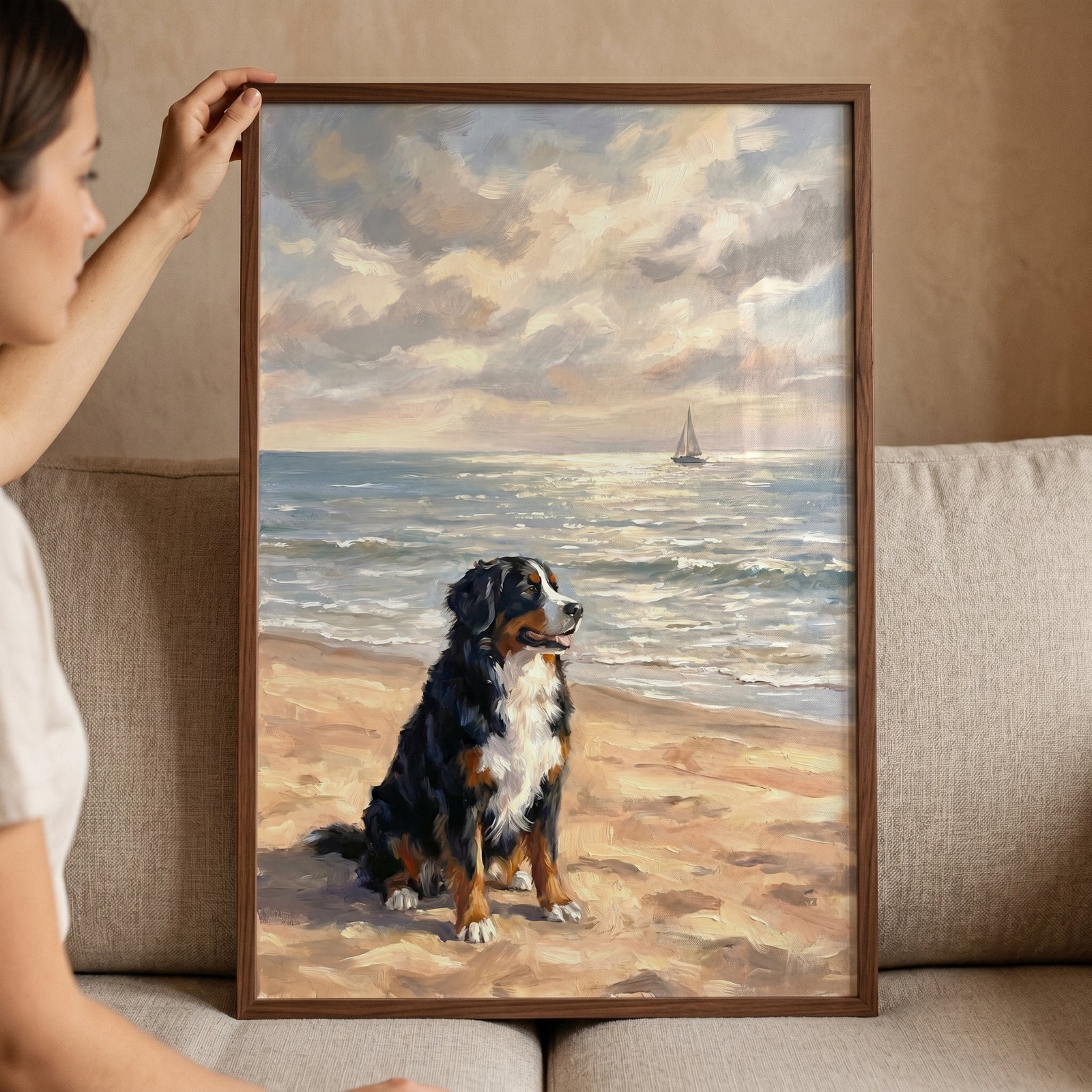 A person holds coastal bernese mountain dog wall art of a dog on a beach with a sailboat on the ocean.