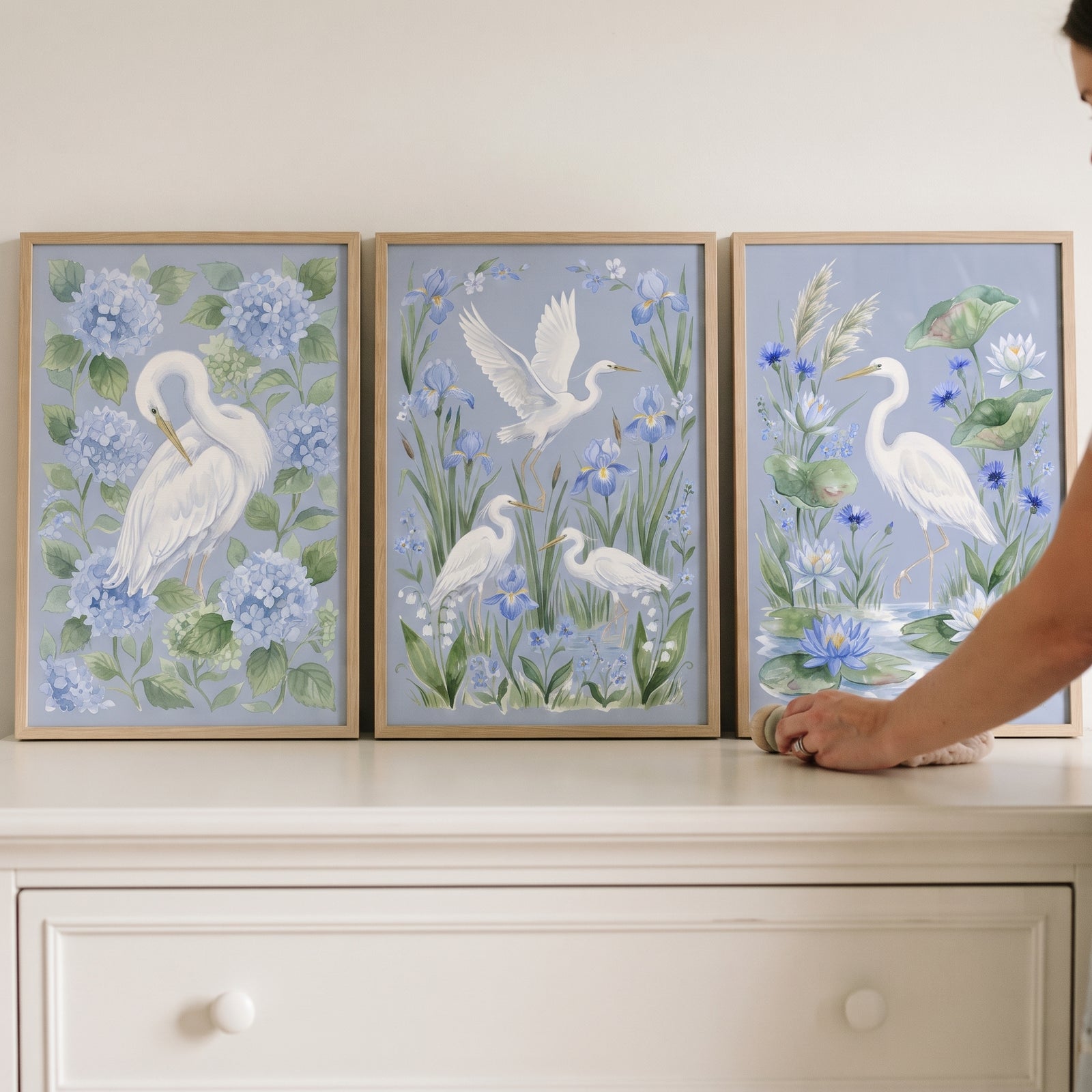 Coastal blue white egret bird wall art set of 3 on a white dresser with floral and foliage backgrounds.