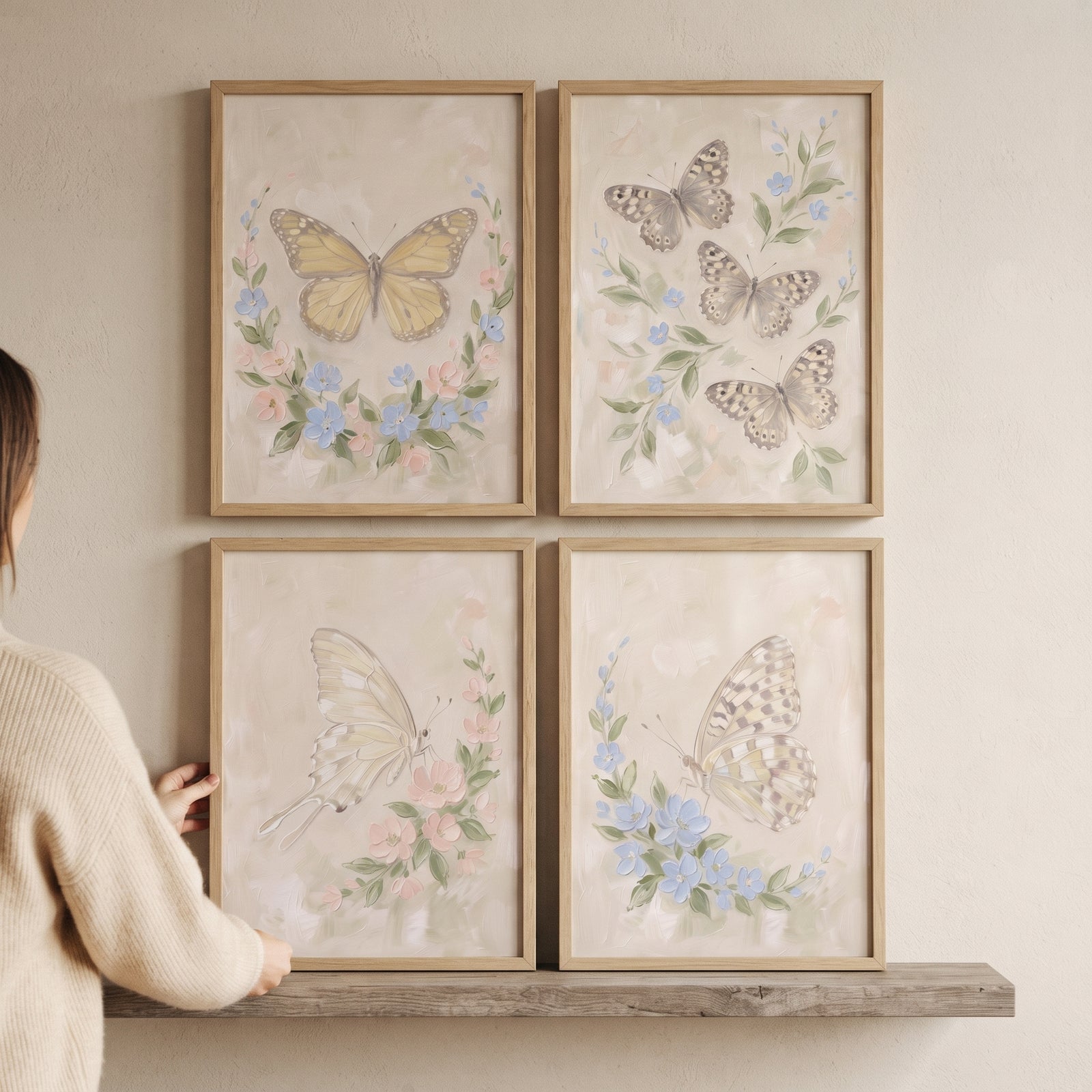 A person adjusts a coastal grandmother floral butterfly wall art set of 4 on a wooden shelf against a neutral wall.
