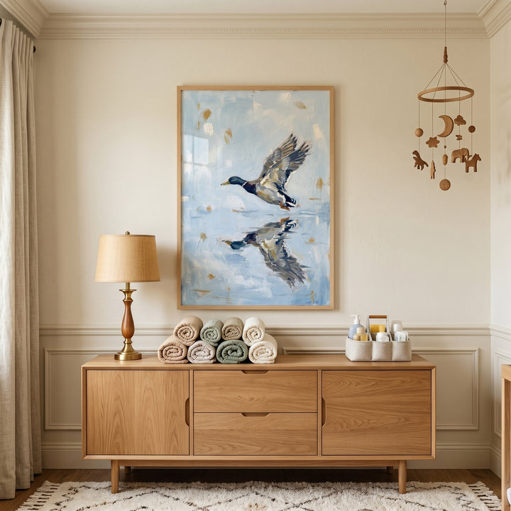 Coastal lakehouse style mallard duck artwork above a wooden sideboard with rolled towels, a lamp, and a hanging mobile.