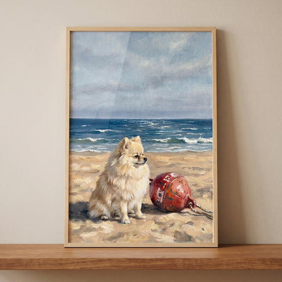 Coastal sandy beach pomeranian dog wall art features a fluffy dog sitting on sand next to a red buoy with ocean waves.