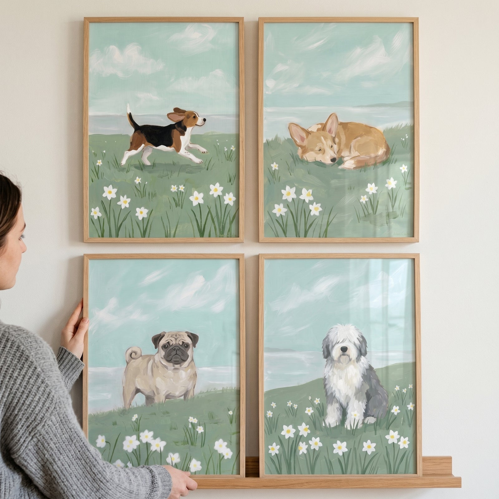 A person displays a coastal spring floral dog wall art set of 4 featuring a beagle, corgi, pug, and sheepdog.