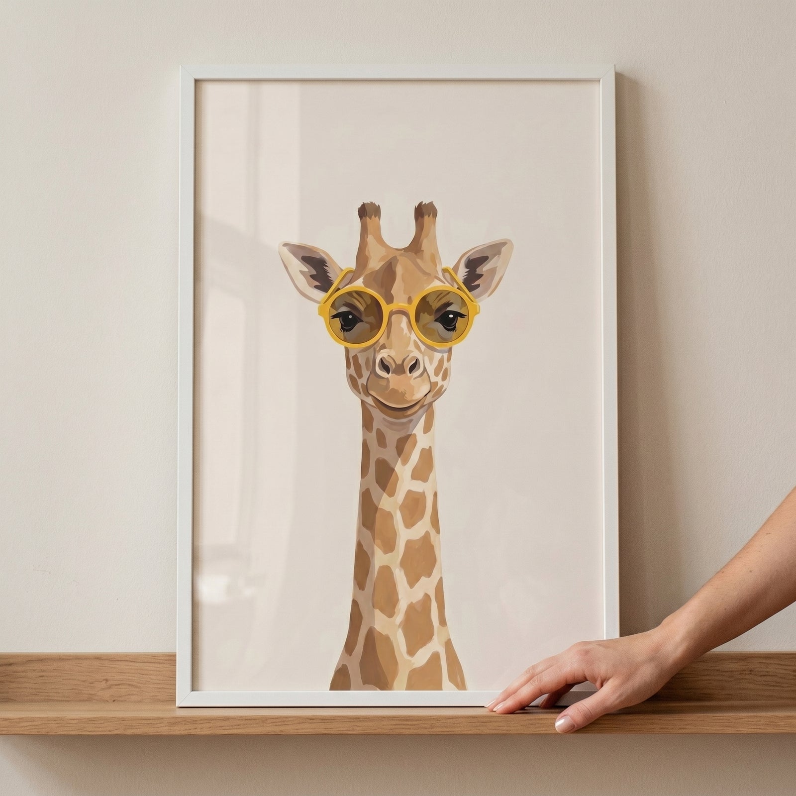 Cool yellow glasses giraffe wall art in a white frame on a wooden shelf with a hand touching the corner.
