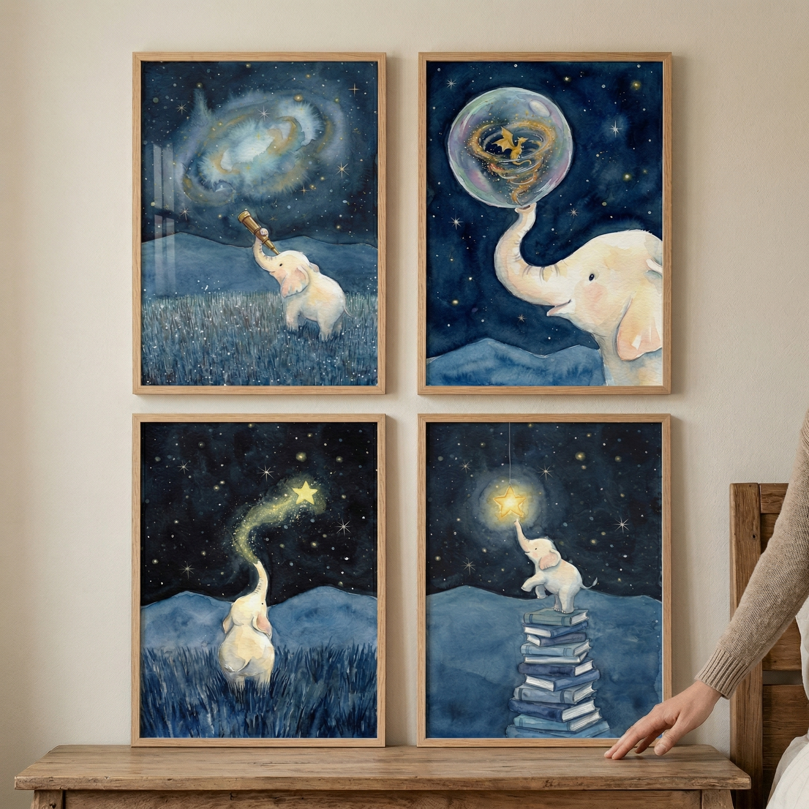 Four framed watercolor-style illustrations in a grid feature a small white elephant. Top left: the elephant views a galaxy through a telescope. Top right: it touches a bubble containing a golden creature. Bottom left: it blows a trail of stardust from its trunk. Bottom right: it stands on a stack of books to reach a hanging star. The night-themed scenes use dark blues and bright yellows. The pieces are held in thin wooden frames above a rustic wooden surface.