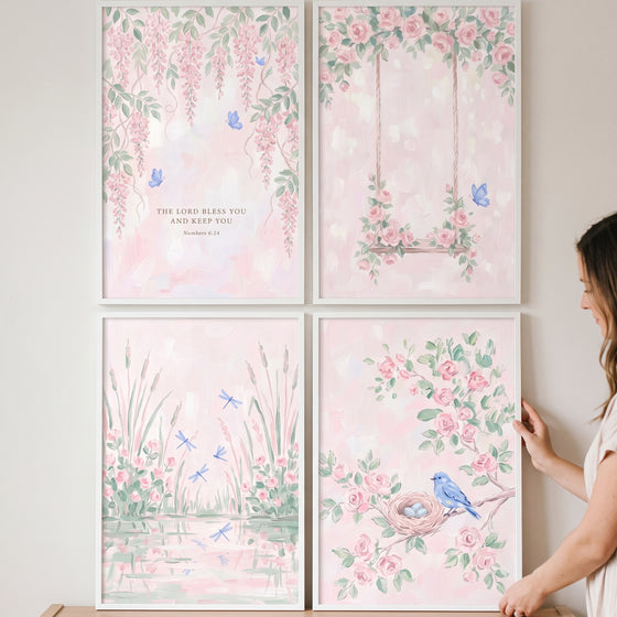 Cottagecore blush watercolor garden print set of 4 with pink flowers, blue birds, and a swing displayed on a wall.