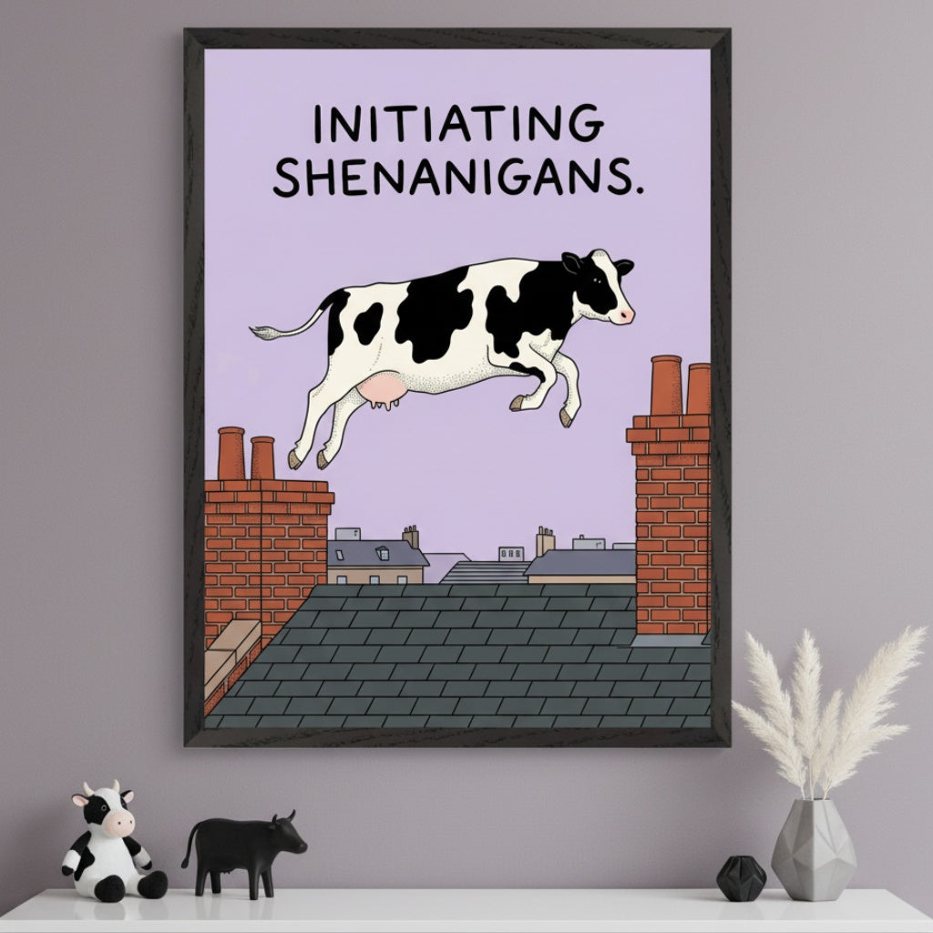 Modern room with a white shelf. A large framed print hangs above the shelf, depicting a cartoon black and white cow jumping over rooftops with "INITIATING SHENANIGANS" text. A plush cow, black cow figurine, and vase with pampas grass are on the shelf.