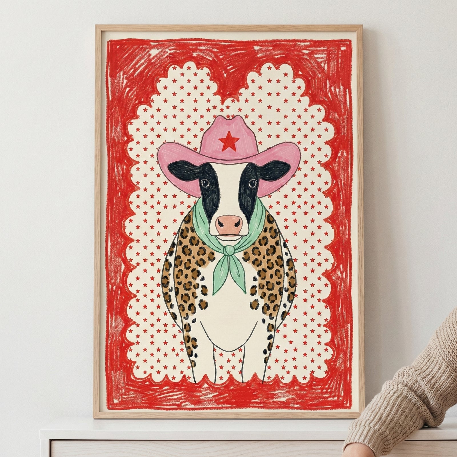 Whimsical illustration of a cow wearing a pink cowboy hat, green scarf, and leopard-print vest, framed with a bold red star-patterned border.