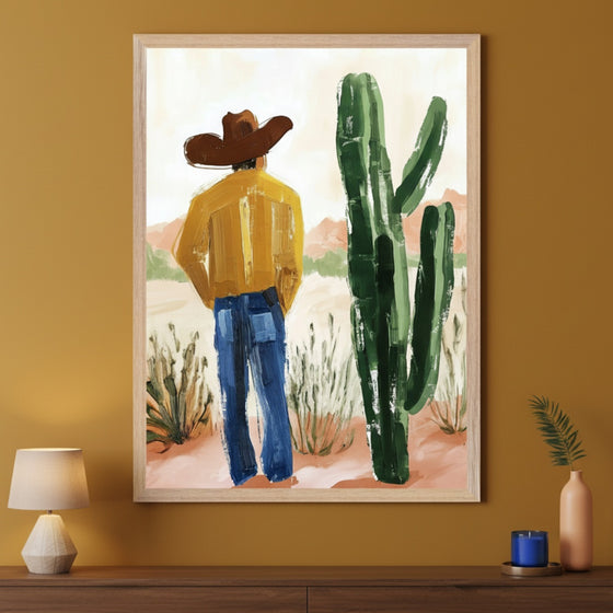 Modern room with a mustard wall and a dark wood console table. A large framed painting hangs centered above the table, depicting a man in a cowboy hat and yellow shirt standing in a desert landscape next to a large cactus, rendered in a brushstroke style.