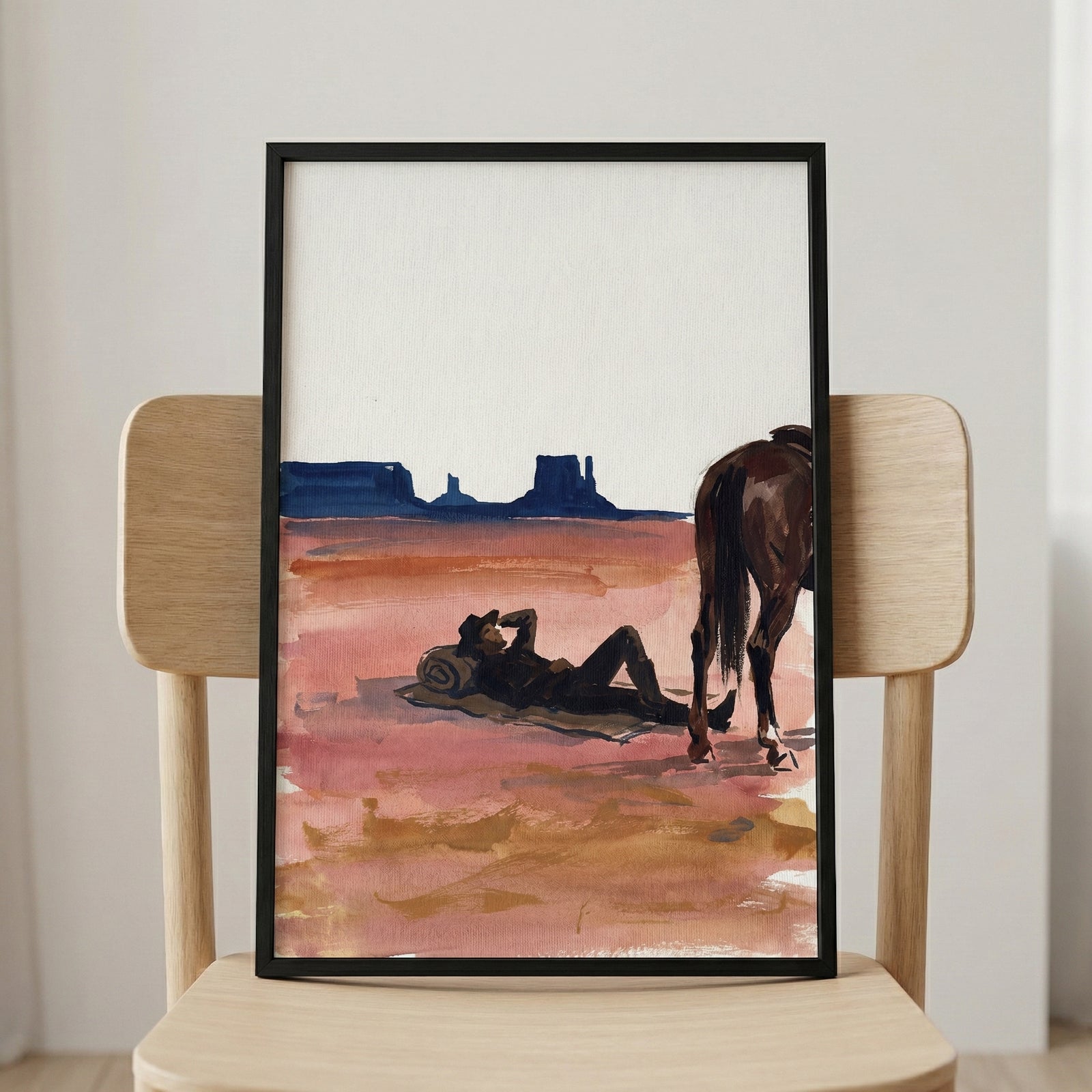 Framed artwork showing a cowboy resting on the desert floor with a rolled blanket under his head, beside his horse. The watercolor-style painting uses warm earth tones and deep blues to evoke a serene western desert landscape.